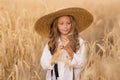 Adorable little girl in a straw hat in wheat field. Child with long blonde wavy hair on countryside landscape with spikelet in Royalty Free Stock Photo