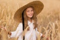 Adorable little girl in a straw hat in wheat field. Child with long blonde wavy hair on countryside landscape with spikelet in Royalty Free Stock Photo