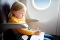Adorable little girl traveling by an airplane. Child sitting by aircraft window and drawing a picture with felt-tip pens. Royalty Free Stock Photo