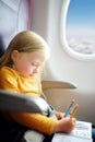 Adorable little girl traveling by an airplane. Child sitting by aircraft window and drawing a picture with felt-tip pens. Royalty Free Stock Photo