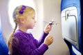 Adorable little girl traveling by an airplane. Child sitting by aircraft window and playing with toy plane. Traveling with kids.