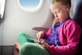 Adorable little girl traveling by an airplane. Child sitting by aircraft window and using a digital tablet during the flight. Royalty Free Stock Photo