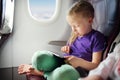 Adorable little girl traveling by an airplane. Child sitting by aircraft window and using a digital tablet during the flight. Royalty Free Stock Photo