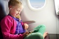 Adorable little girl traveling by an airplane. Child sitting by aircraft window and using a digital tablet during the flight. Royalty Free Stock Photo