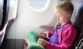 Adorable little girl traveling by an airplane. Child sitting by aircraft window and using a digital tablet during the flight. Royalty Free Stock Photo