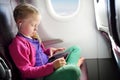 Adorable little girl traveling by an airplane. Child sitting by aircraft window and using a digital tablet during the flight. Royalty Free Stock Photo