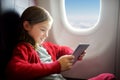 Adorable little girl traveling by an airplane. Child sitting by aircraft window and using a digital tablet during the flight. Royalty Free Stock Photo