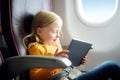 Adorable little girl traveling by an airplane. Child sitting by aircraft window and using a digital tablet during the flight. Royalty Free Stock Photo