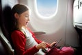 Adorable little girl traveling by an airplane. Child sitting by aircraft window and using a digital tablet during the flight. Royalty Free Stock Photo