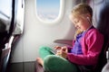 Adorable little girl traveling by an airplane. Child sitting by aircraft window and using a digital tablet during the flight. Royalty Free Stock Photo