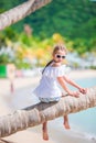 Adorable little girl at tropical beach sitting on palm tree during summer vacation Royalty Free Stock Photo