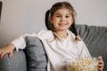 Adorable little girl watching TV at home and laughs. Cute girl eating popcorn. Holiday mood Royalty Free Stock Photo