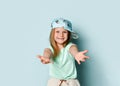 Adorable little girl wearing cap with pineapple pattern extending her arms with smile going to embrace a spectator. Studio shot