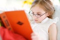 Adorable little girl wearing eyeglasses reading a book in white living room Royalty Free Stock Photo