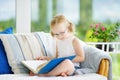 Adorable little girl wearing eyeglasses reading a book in white living room Royalty Free Stock Photo