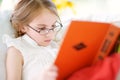 Adorable little girl wearing eyeglasses reading a book in white living room Royalty Free Stock Photo