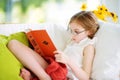 Adorable little girl wearing eyeglasses reading a book in white living room on summer day Royalty Free Stock Photo