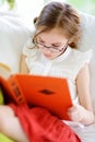 Adorable little girl wearing eyeglasses reading a book in white living room on summer day Royalty Free Stock Photo