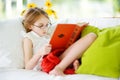 Adorable little girl wearing eyeglasses reading a book in white living room on summer day Royalty Free Stock Photo