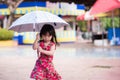 Adorable little girl wearing a red dress with watermelon prints walks an umbrella on a drizzly day in the rainy season. Royalty Free Stock Photo