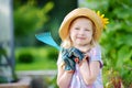 Adorable little girl wearing straw hat and childrens garden gloves playing with her toy garden tools in a greenhouse Royalty Free Stock Photo