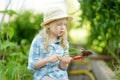 Adorable little girl wearing straw hat playing with her toy garden tools in a greenhouse on sunny summer day Royalty Free Stock Photo