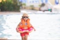 Adorable little girl wearing sunglasses, inflatable over-sleeves floats and inflatable donut float ring, swimming pool at the Royalty Free Stock Photo