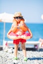 Adorable little girl wearing sunglasses, inflatable over-sleeves floats and inflatable donut float ring, sea coast at the Royalty Free Stock Photo