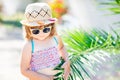 Close-up portrait of adorable little girl at the tropical resort, hiding behind the palm at the sunny summer day Royalty Free Stock Photo