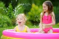 Adorable little girls playing in inflatable baby pool. Happy kids splashing in colorful garden play center on hot summer day. Royalty Free Stock Photo