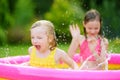 Adorable little girls playing in inflatable baby pool. Happy kids splashing in colorful garden play center on hot summer day. Royalty Free Stock Photo