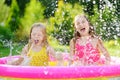 Adorable little girls playing in inflatable baby pool. Happy kids splashing in colorful garden play center on hot summer day. Royalty Free Stock Photo