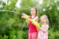 Adorable little girls playing with water guns on hot summer day. Cute children having fun with water outdoors. Royalty Free Stock Photo