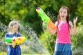 Adorable little girls playing with water guns on hot summer day. Cute children having fun with water outdoors. Royalty Free Stock Photo