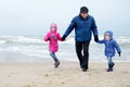 Adorable little girls and their grandpa playing by the ocean on winter day