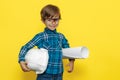 Adorable little kid boy engineer or architect holding protective helmet and construction plan over yellow background. Royalty Free Stock Photo