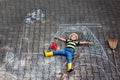 Adorable little kid boy playing with colorful chalks and painting big tractor picture on asphalt. Happy preschool child