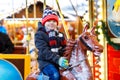 Adorable little kid boy riding on a carousel horse at Christmas funfair or market, outdoors. Royalty Free Stock Photo