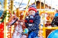 Adorable little kid boy riding on a merry go round carousel horse at Christmas funfair or market, outdoors. Happy child Royalty Free Stock Photo