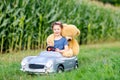 Adorable little kid girl sitting in big vintage old toy car and having fun with playing with big plush toy bear, Royalty Free Stock Photo