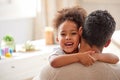 Adorable little mixed race girl with curly afro hair smiling and hugging her father at home. Hispanic father bonding and Royalty Free Stock Photo