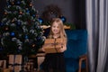 adorable little preschool blonde girl in a black dress holding new years present near a christmas tree. dark loft room Royalty Free Stock Photo