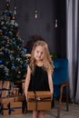 adorable little preschool blonde girl in a black dress holding new years present near a christmas tree. dark loft room Royalty Free Stock Photo