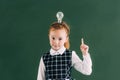 adorable little redhead schoolgirl with light bulb on head pointing up with finger and looking Royalty Free Stock Photo