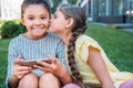 adorable little schoolgirl with smartphone looking at camera while her friend kissing