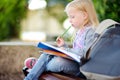 Adorable little schoolgirl studying outdoors on bright autumn day. Young student doing her homework. Education for small kids. Royalty Free Stock Photo