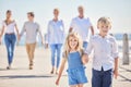 Adorable little sibling brother and sister holding hands while walking ahead on a seaside promenade while their parents Royalty Free Stock Photo