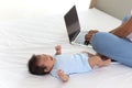 Adorable little sweet newborn baby girl crying on white bed near her mom using notebook laptop computer, cute infant with her busy Royalty Free Stock Photo