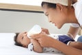 Adorable little sweet newborn baby girl lying on white bed with her mother holding milk bottle for feeding baby, cute infant with Royalty Free Stock Photo