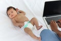 Adorable little sweet newborn baby girl lying on white bed near her mom using notebook laptop computer, cute infant with her busy Royalty Free Stock Photo